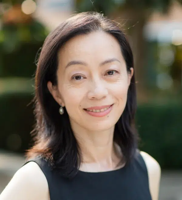 A woman with shoulder-length dark hair, wearing a sleeveless black top, is seen smiling in an outdoor setting near Redmond Ridge Orthodontics.