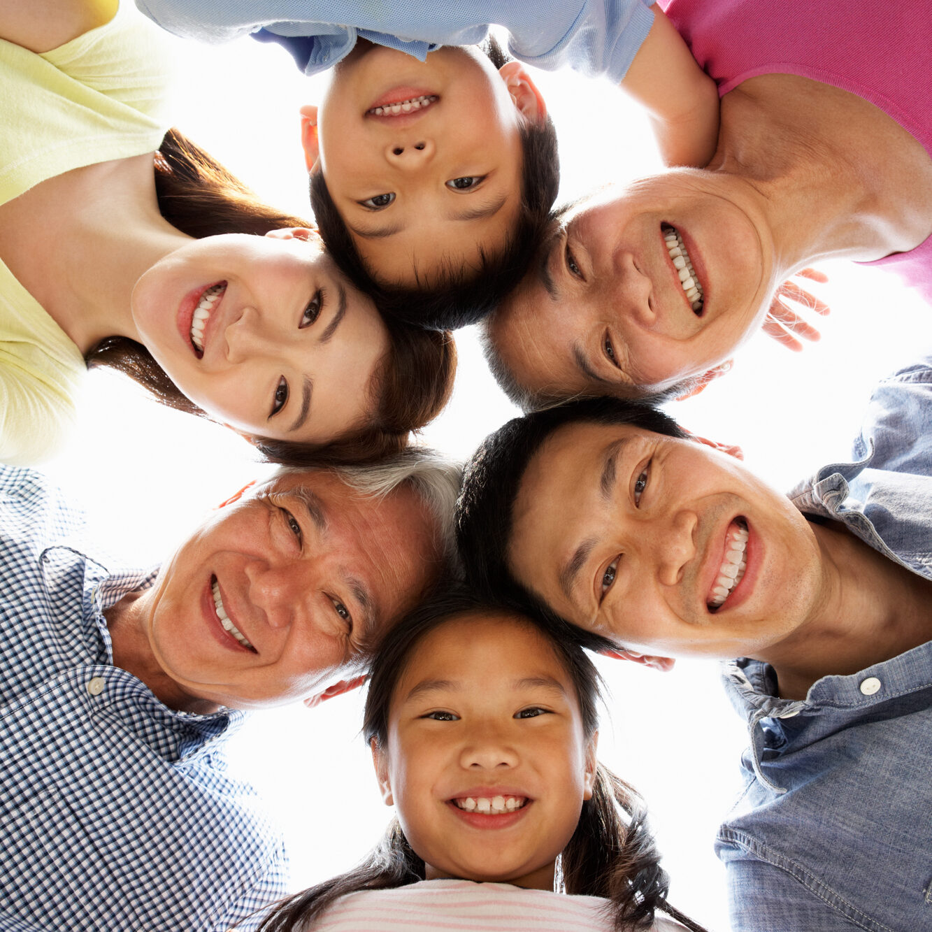 Six people of varying ages, including children and adults, form a circle and smile down at the camera. They are grouped closely together and appear to be a family, showcasing the beautiful smiles achieved with help from Redmond Ridge Orthodontics.
