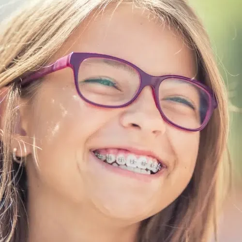 A child with long brown hair, purple glasses, and braces from Redmond Ridge Orthodontics smiles widely.