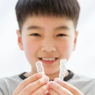 A child smiles while holding two dental aligners in their hands, showcasing the exceptional care provided by Redmond Ridge Orthodontics.