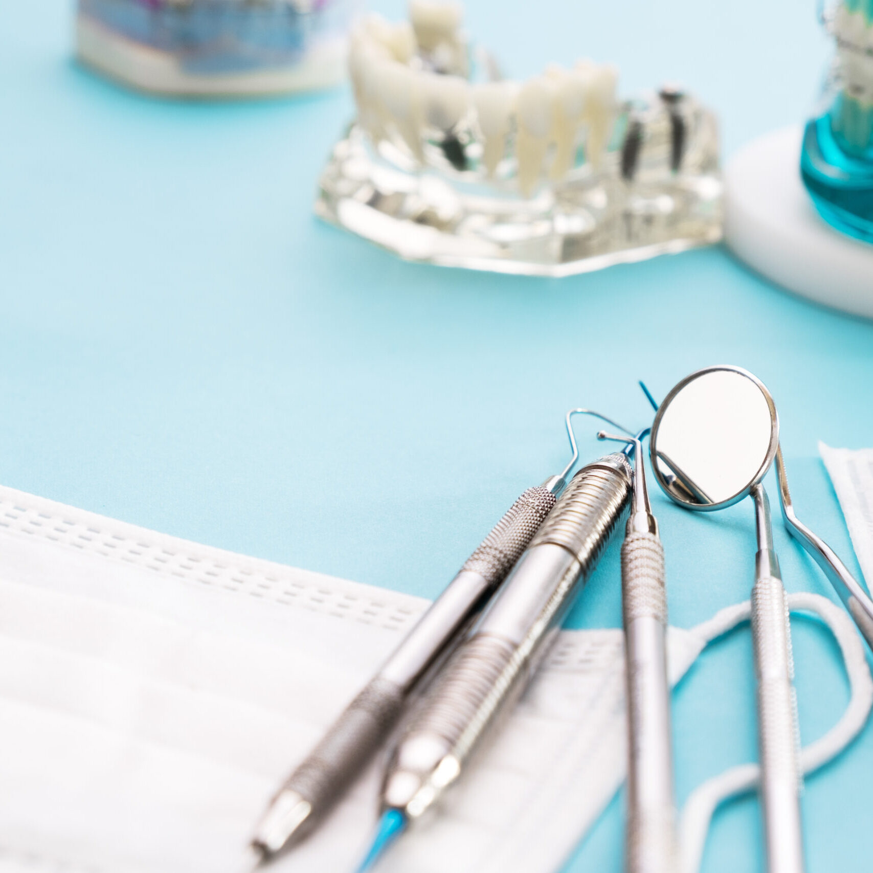 Dental tools including a mirror, probe, and explorer are placed on a white face mask. In the background, there are models of teeth on a blue surface, showcasing the precision instruments used at Redmond Ridge Orthodontics.